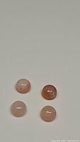 Four natural round cabochon pink opal gemstones arranged in a square on a light surface.
