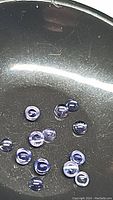 Photo showing multiple small round cabochon cut purple iolite gemstones on a reflective surface, highlighting the cabochon shape and purple coloration.