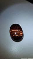 Oval cabochon cut red tiger's eye gemstone displaying bright red and golden chatoyancy effect on a smooth polished surface.