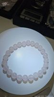 Close-up top view of the natural rose quartz bracelet showing polished round beads arranged in a circular bracelet shape on white background.