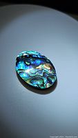 Close-up image of the oval cabochon abalone doublet gemstone showing vivid iridescent colors and natural patterns on the stone's surface.