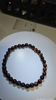 Photo of the red tigerseye bead stretchy bracelet on a white background, showing the banded pattern on the beads.