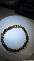 Natural tigerseye bead bracelet laid flat on a round white surface under light showing reflective chatoyancy of beads.