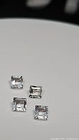 Four square cut natural white topaz gemstones on a white surface, showcasing clarity and calibrated size.