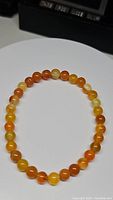 Photo showing natural yellow to orange agate round beads forming a stretchy bracelet, laid flat on a white surface with a black object in the background.