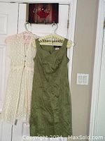 Green sleeveless Algo dress and white sleeveless cardigan hanging on hangers.