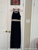Black sleeveless evening dress hanging on a decorative hanger, showing bling on neckline and waist band, full length visible