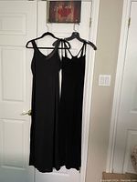 Photo of two black evening dresses hanging on wall showing full length and strap details