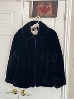 Front view of black faux fur jacket on hanger showing collar and full zipper.