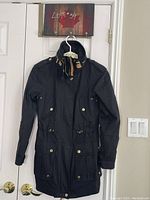 Front view of black Vera Moda jacket hanging on a hanger, showing high collar, buttoned epaulets, four flap pockets with snap buttons, and front zipper/button closure.