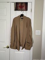 Front view of the taupe jersey car coat hanging on a door, showing its open front, ribbed cuffs and hem, and relaxed fit.