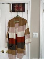 Front view of multi-coloured striped long sweater car coat hanging on green hanger on white door.