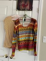 Both garments hanging on hangers on a white door, cardigan in front showing full pattern, yellow and white top behind partially visible.