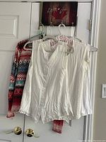 Four garments hanging: one multi-coloured cardigan with red, black, white, and blue geometric pattern, three white sleeveless tops in medium size
