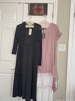 Photo of pink dress and black/grey long coat hanging on hangers on a door.