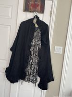 Large black shawl with scalloped ruffled edges and zebra print lining visible, hanging on door