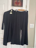 Black sheer dress pants and plain black car coat hanging on a door, shown front view