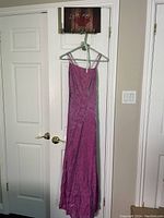 Pink sleeveless evening dress with spaghetti straps hanging on a hanger against white double doors. Side zipper visible.