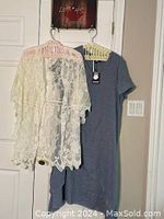 Photo of blue tunic dress and white lace shawl hanging on hangers against door