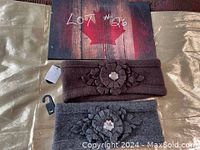 Two wool headbands/ear warmers laid out flat, one purple and one grey, each featuring a sewn floral appliqué with a central gem.