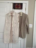 Photo of the cream long vest and light taupe sweater hanging side by side on hangers.