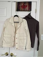 White jean jacket and grey taupe turtle neck hanging on a door showing full front.