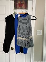 Black casual pants, royal blue leggings, and blue sleeveless boho top hanging on a door