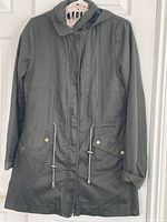 Hunter green long women's coat by Long Tall Sally hanging on door, front view with pockets, drawstring waist cords, and hood visible.