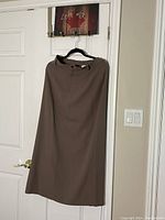 Front view of taupe pencil maxi skirt by Part Two hanging on a door, showing full length and slit at the back.