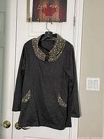 Front view of dark gray long sleeve Lavena shirt dress with floral patterned cowl neck and pocket trims, hanging on black hanger on door knob.