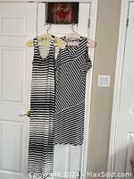 Two striped dresses hanging side by side on hangers on a wall, showing full length and neckline details of both dresses.