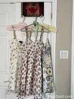 Three baby doll sun dresses hanging on pastel-colored hangers on a door, showcasing varied floral and dot patterns and soft colors.