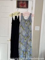 Two maxi length sun dresses hanging on hangers on a door; one is black and the other is blue floral.