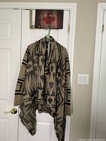 Front view of taupe and black geometric patterned Peruvian style sweater, showing asymmetrical hem and loose fit