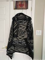 Front view of the sweater vest hanging on a hanger showing the overall pattern and draped open front design.