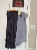Photo showing blue Lavina top hanging with black Casa Donna pleated pants, both on hangers with tags attached
