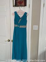 Full length front view of turquoise evening dress hanging on hanger against white door.