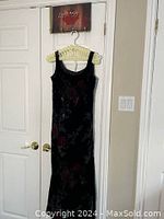 Front view of sleeveless dark velvet evening dress with floral design, hanging on a hanger against a door.