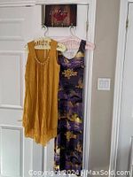 Two sleeveless dresses hanging on plastic hangers on a door: the left is yellow with faux pearls along neckline, the right is a purple and yellow floral sun dress.