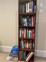 Books arranged on wooden bookshelf and additional books stacked on floor next to it