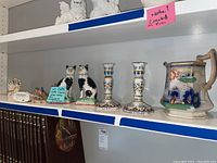 Image showing multiple figurines including cat figures, numbered Rowen candlesticks, and ceramic pitcher on display shelf