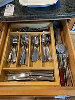 Drawer organizer with sections containing forks, spoons, butter knives, and various cooking and serving utensils including a wooden spoon and a ladle.