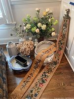 Photo showing faux flower arrangements in vases, ceramic wash bin, ceramic and metal trays, and embroidered tapestries laid out