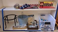 Photo of shelf with folded American flags, Duraflame firestarters box, a metal bucket, black cast iron stand, and bins containing ropes and various small hardware items