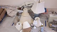 Overview of lamps and various lamp shades laid on floor near rolls of fabric and a sewing machine, showing overall lot contents.