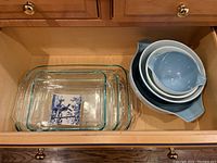 Drawer containing three clear rectangular glass baking dishes and three nested Pyrex mixing bowls in blue and white with vintage pattern designs
