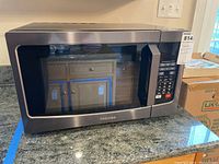 Front and top angle photo showing stainless steel Toshiba microwave on granite countertop with control panel and door window visible.