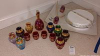 Full set showing multiple small colored glass cups, jars, and one decanter with stopper on the floor.