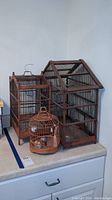Three birdcages of varying sizes and styles displayed together on a surface.