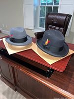 Two vintage men's fedora hats on a wooden desk, displayed side by side showing overall look and crown shapes